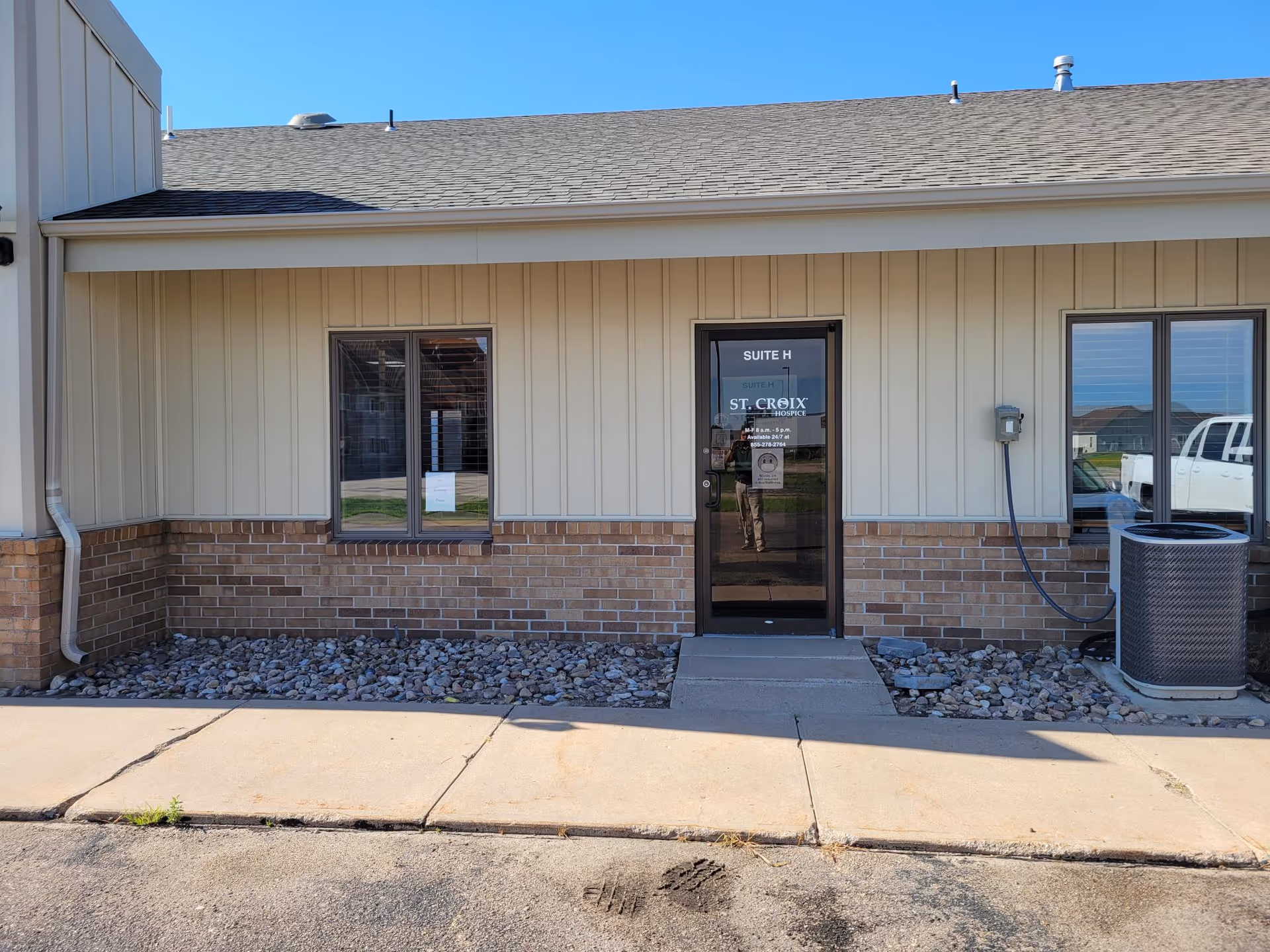 Front entrance of St. Croix Hospice with a glass door labeled Suite H and brick exterior.