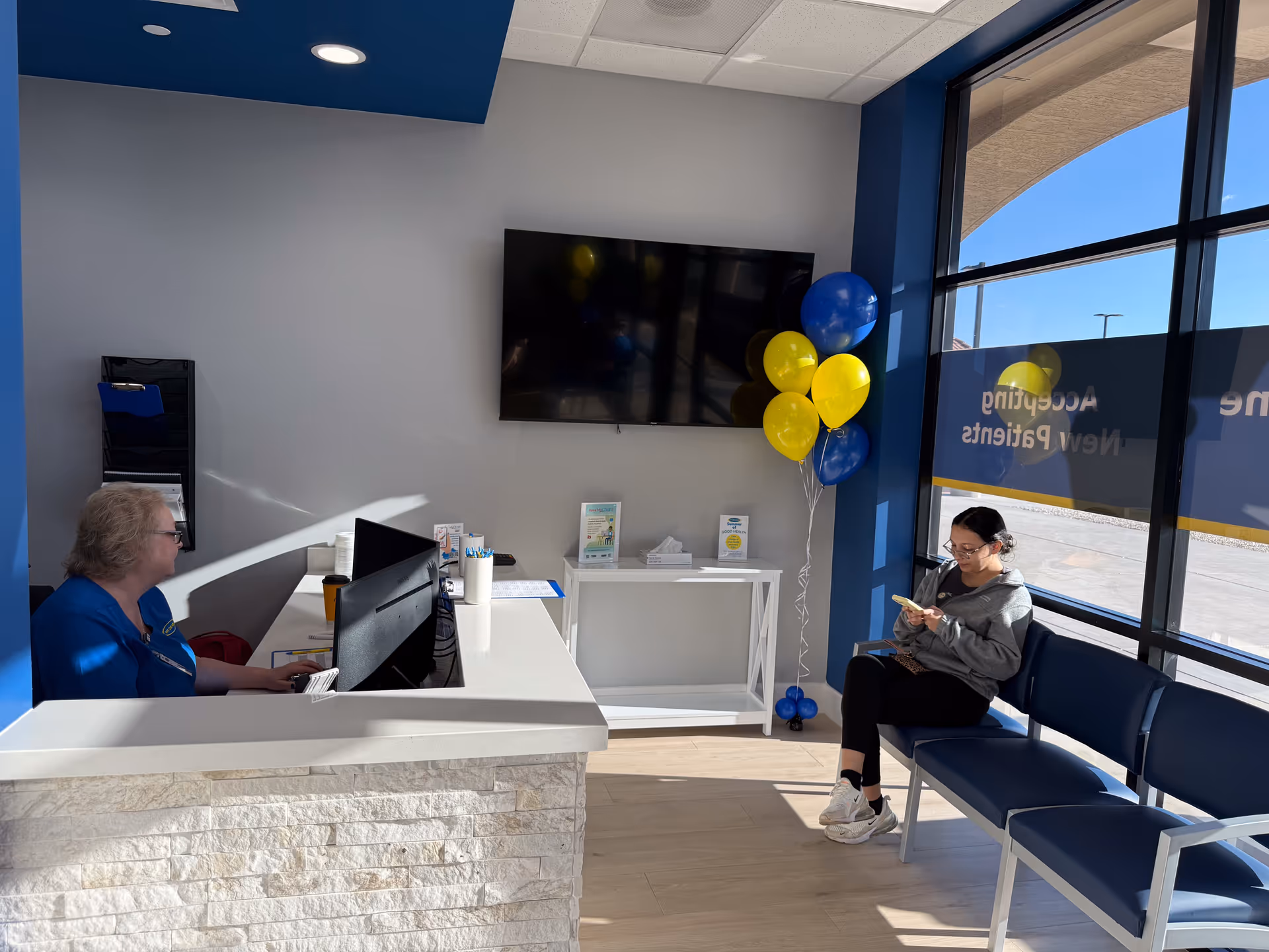 Reception area with a staff member at a desk and a resident seated near balloons.