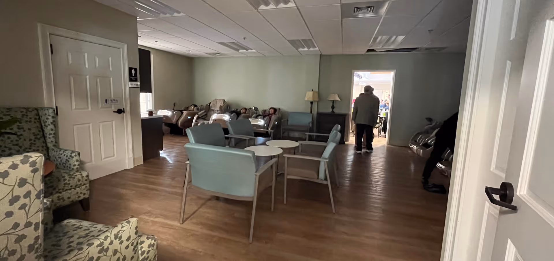 A spacious senior living lounge with light blue chairs and small round tables.