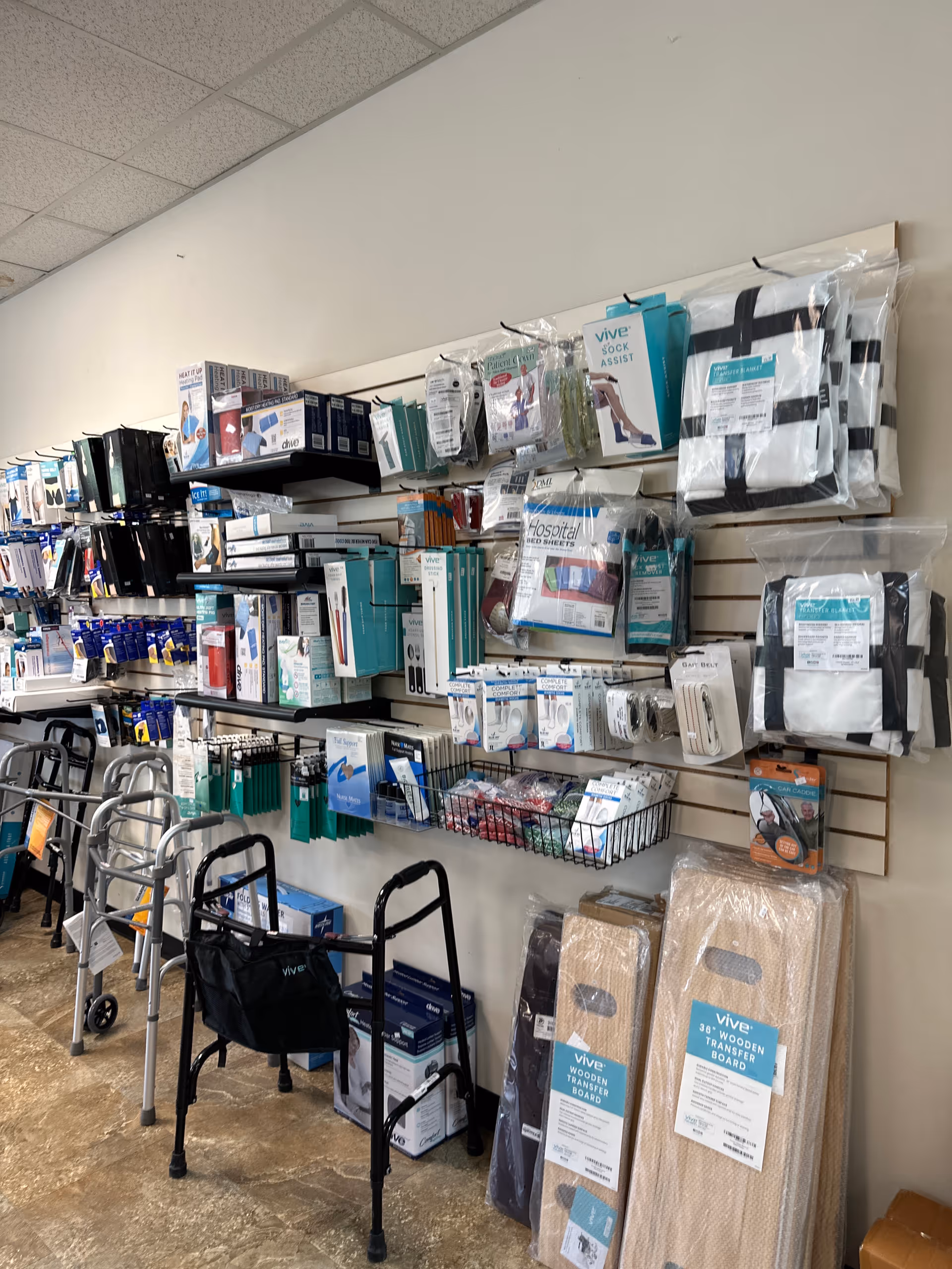 Indoor aisle with medical supplies and mobility aids arranged on wall-mounted display shelves.