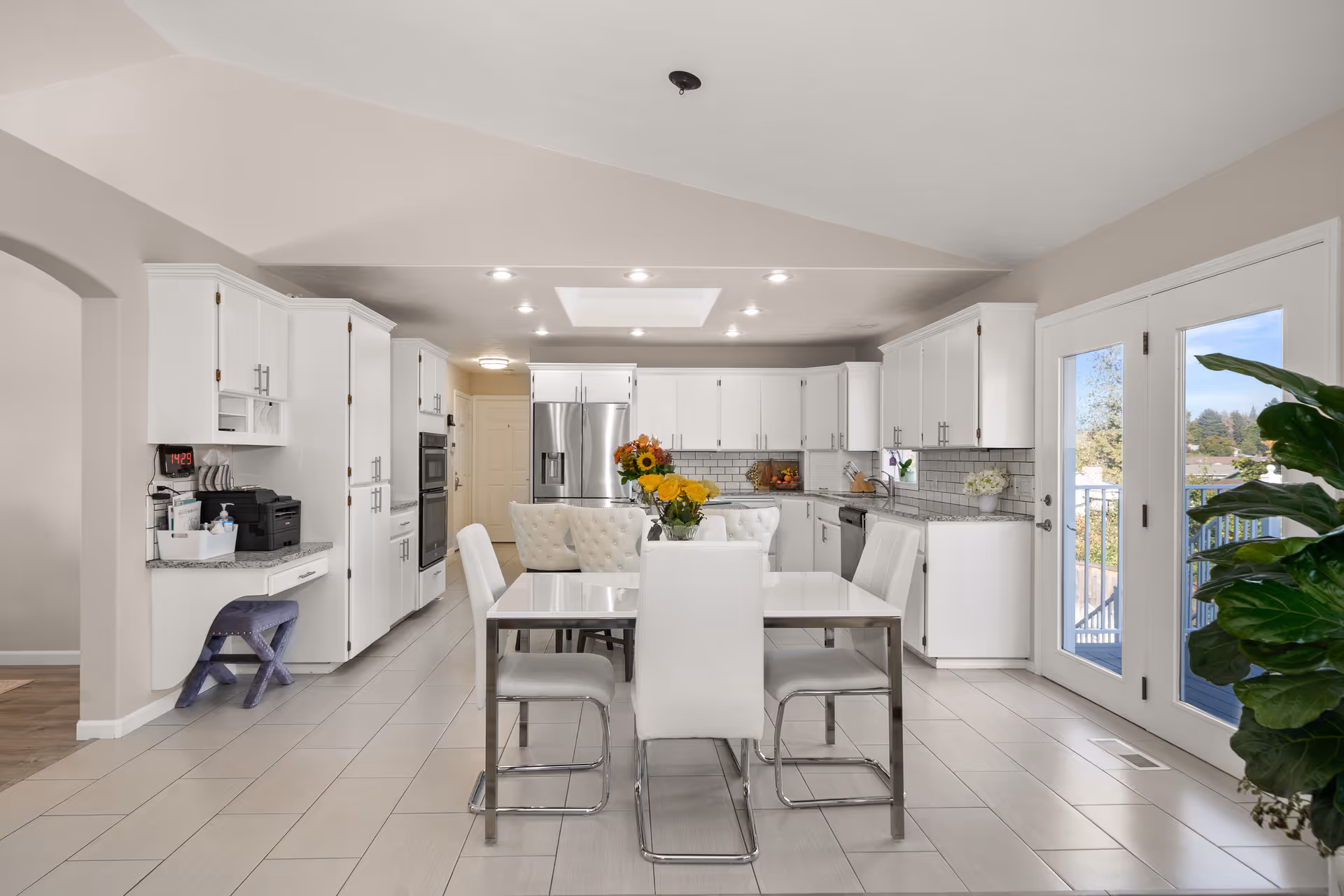 Bright modern kitchen and dining area with white cabinetry, a table, and doors to the outdoors.