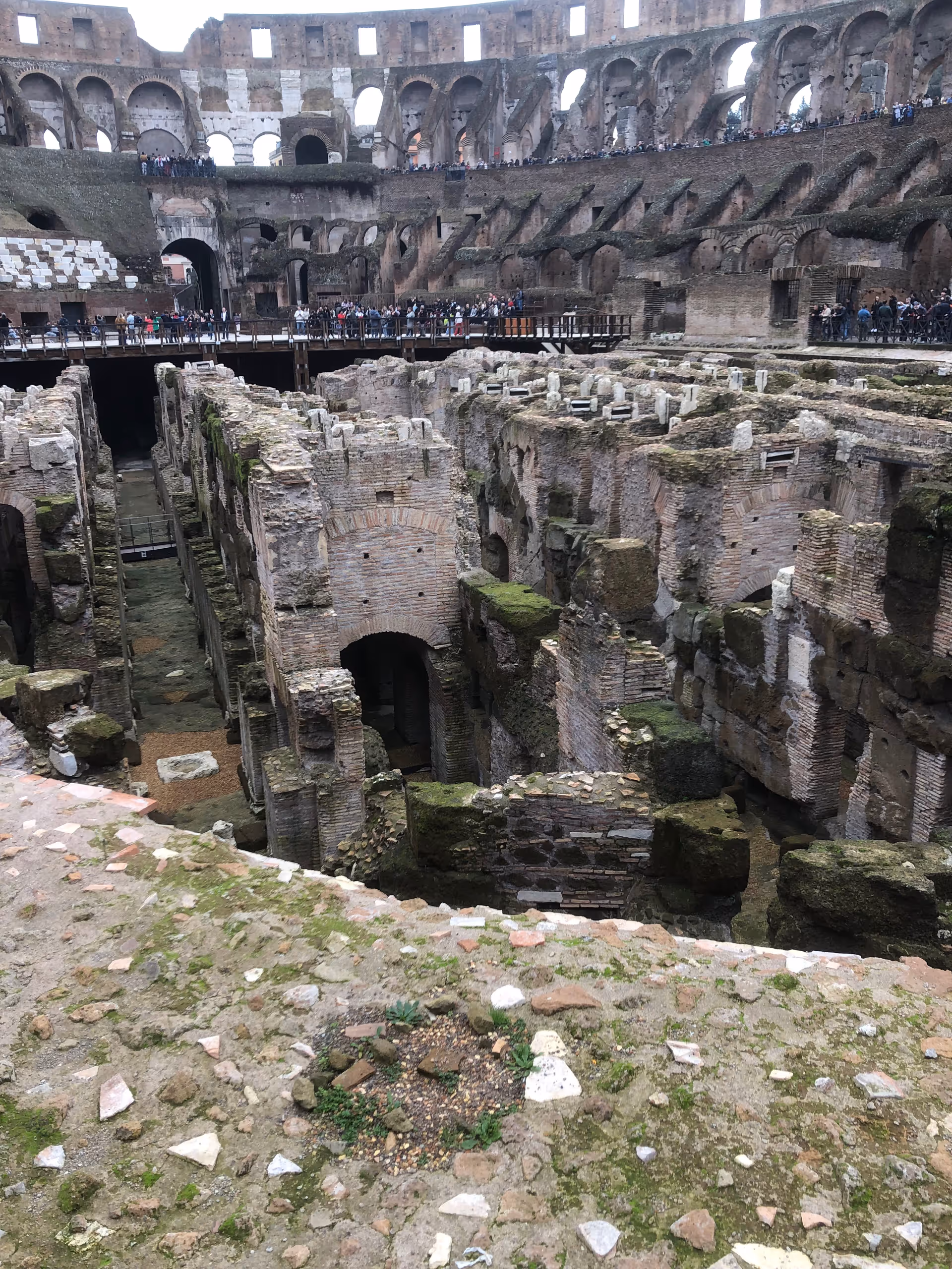 Ancient Colosseum exterior ruins with arches and groups of tourists.