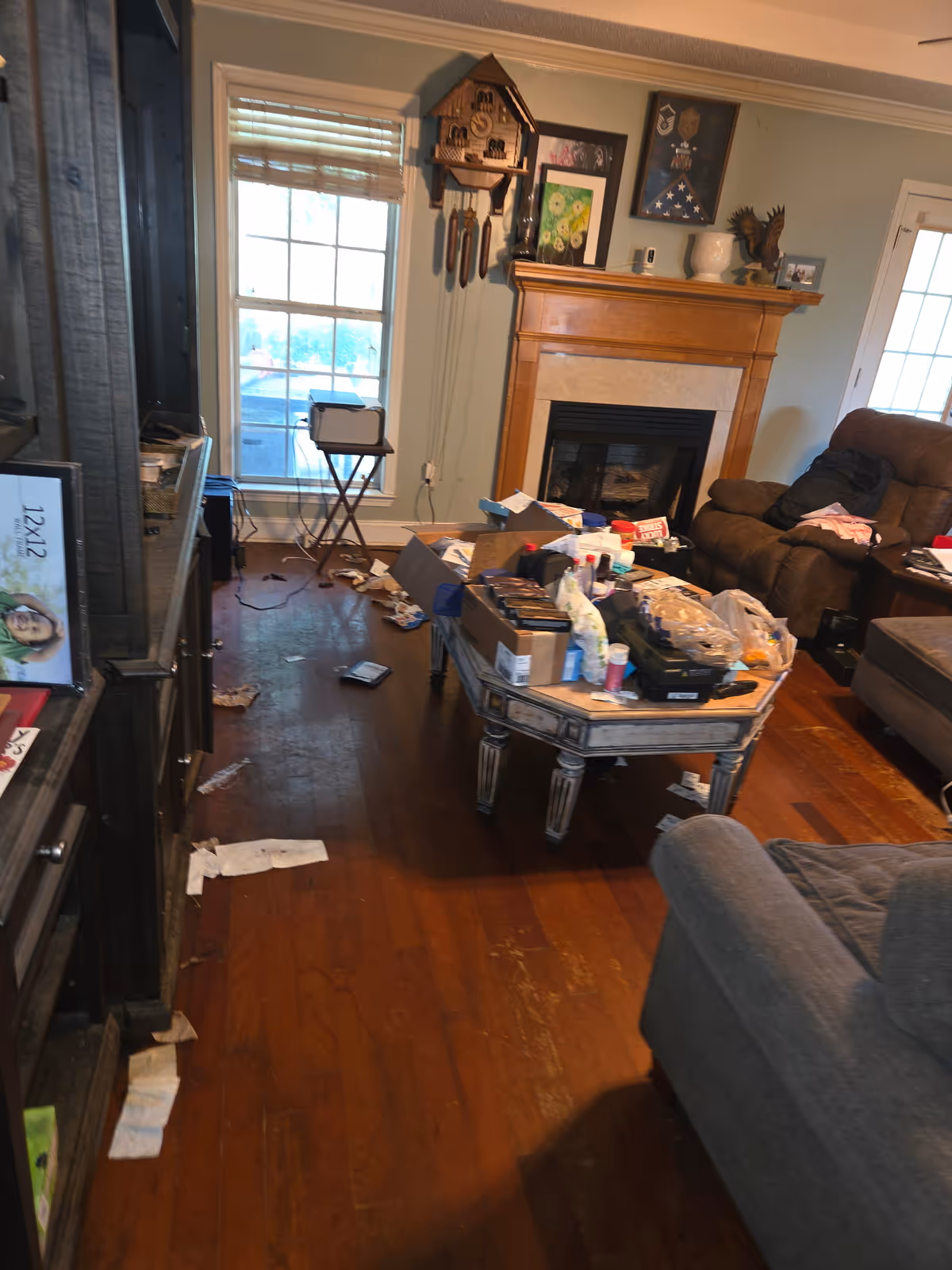 Messy living room with cluttered coffee table, scattered papers, and a couch by a fireplace.
