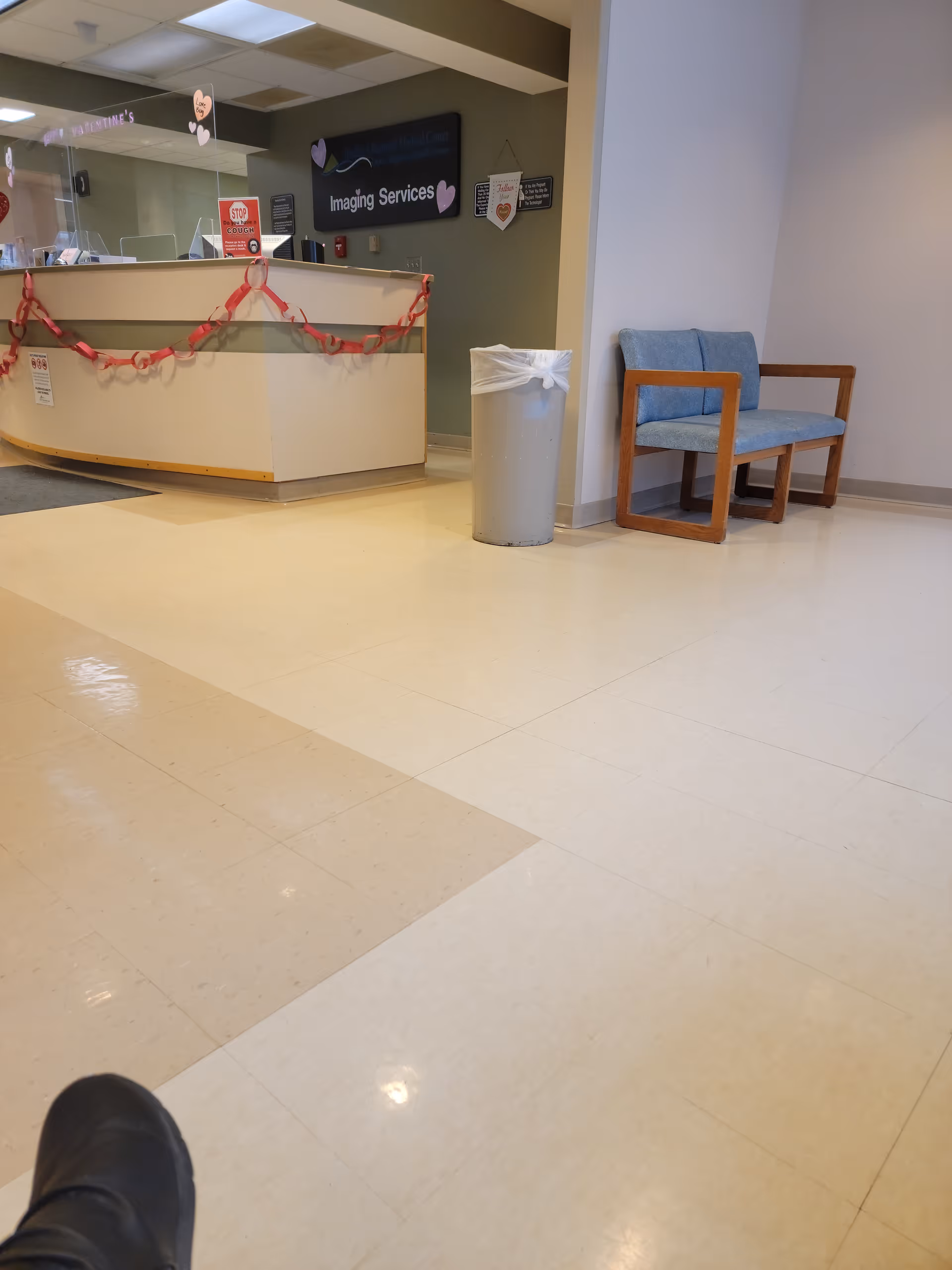 Reception desk with pink garlands, a trash can, and blue chairs in a hospital lobby.