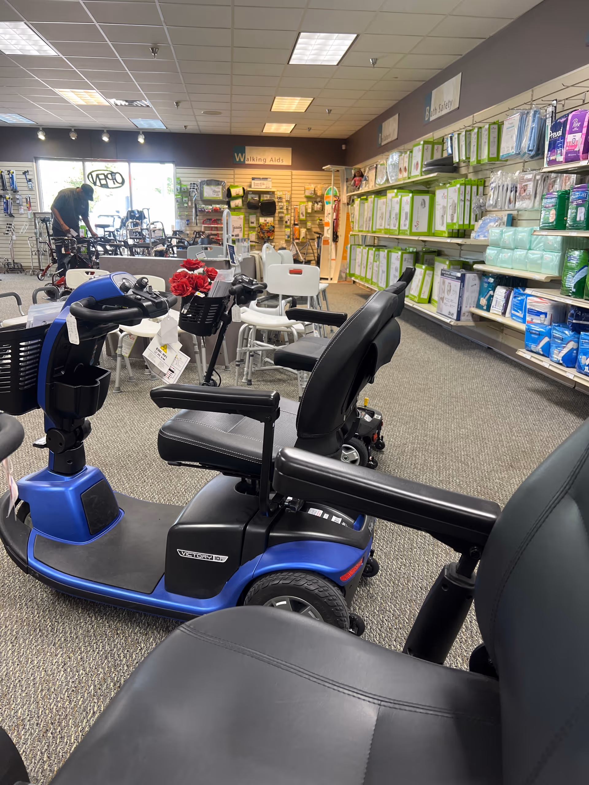 Blue mobility scooter display in a medical supply store, with shelves and seating in the background.