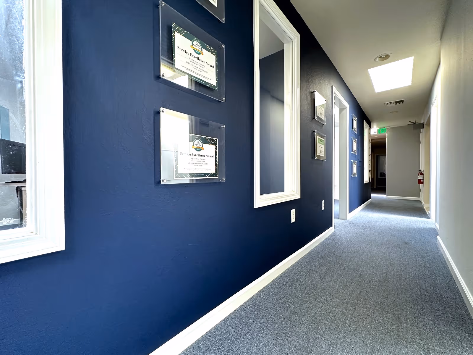 Blue hallway in a senior living facility with framed wall plaques.