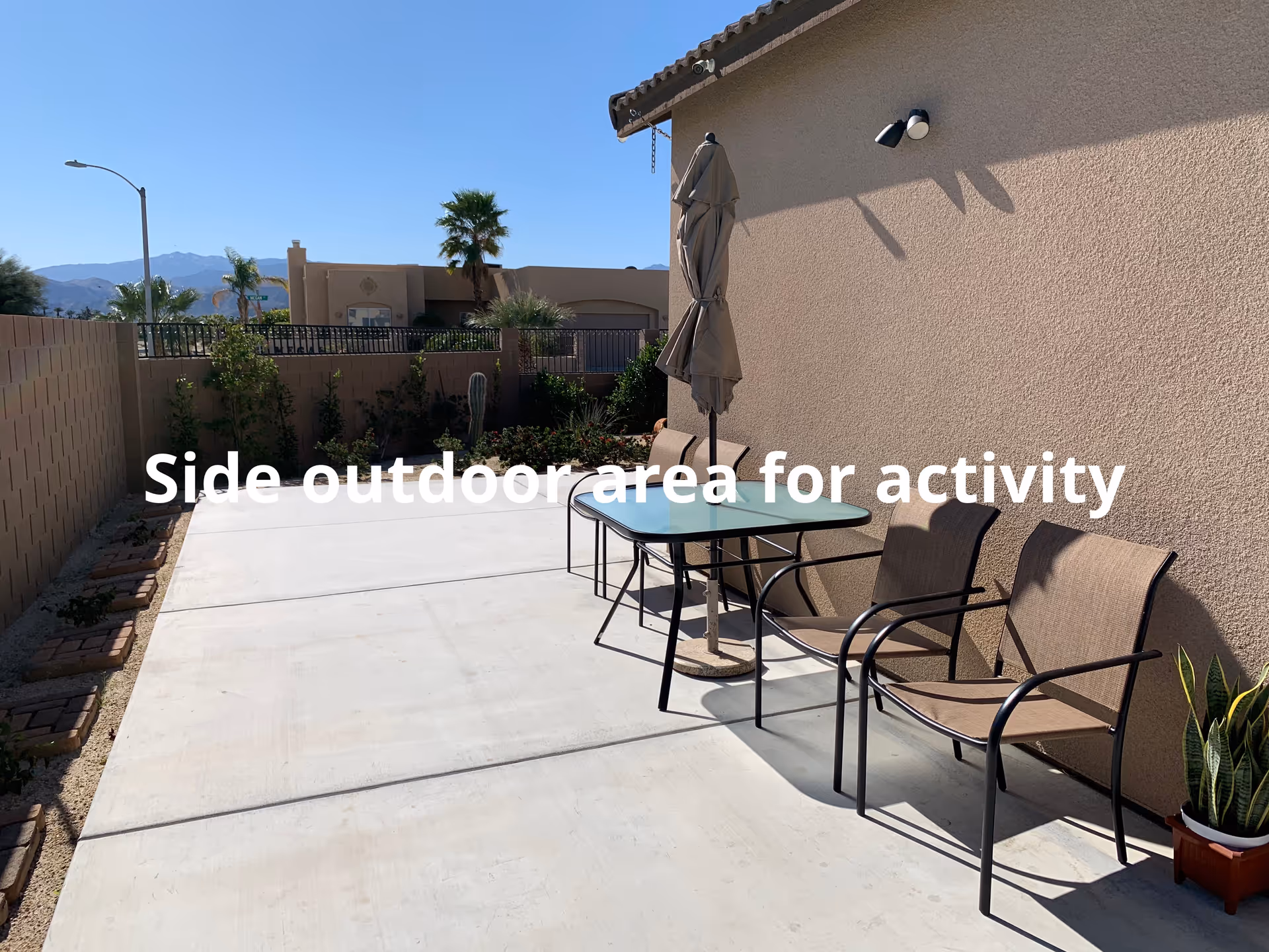 Side outdoor patio with a table, chairs, and an umbrella beside a beige building.