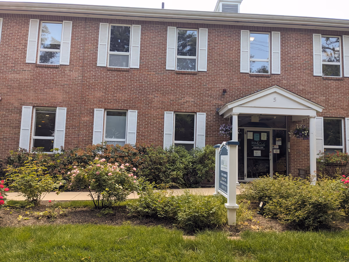 Brick senior living facility exterior with white shutters, entrance porch, and landscaped shrubs