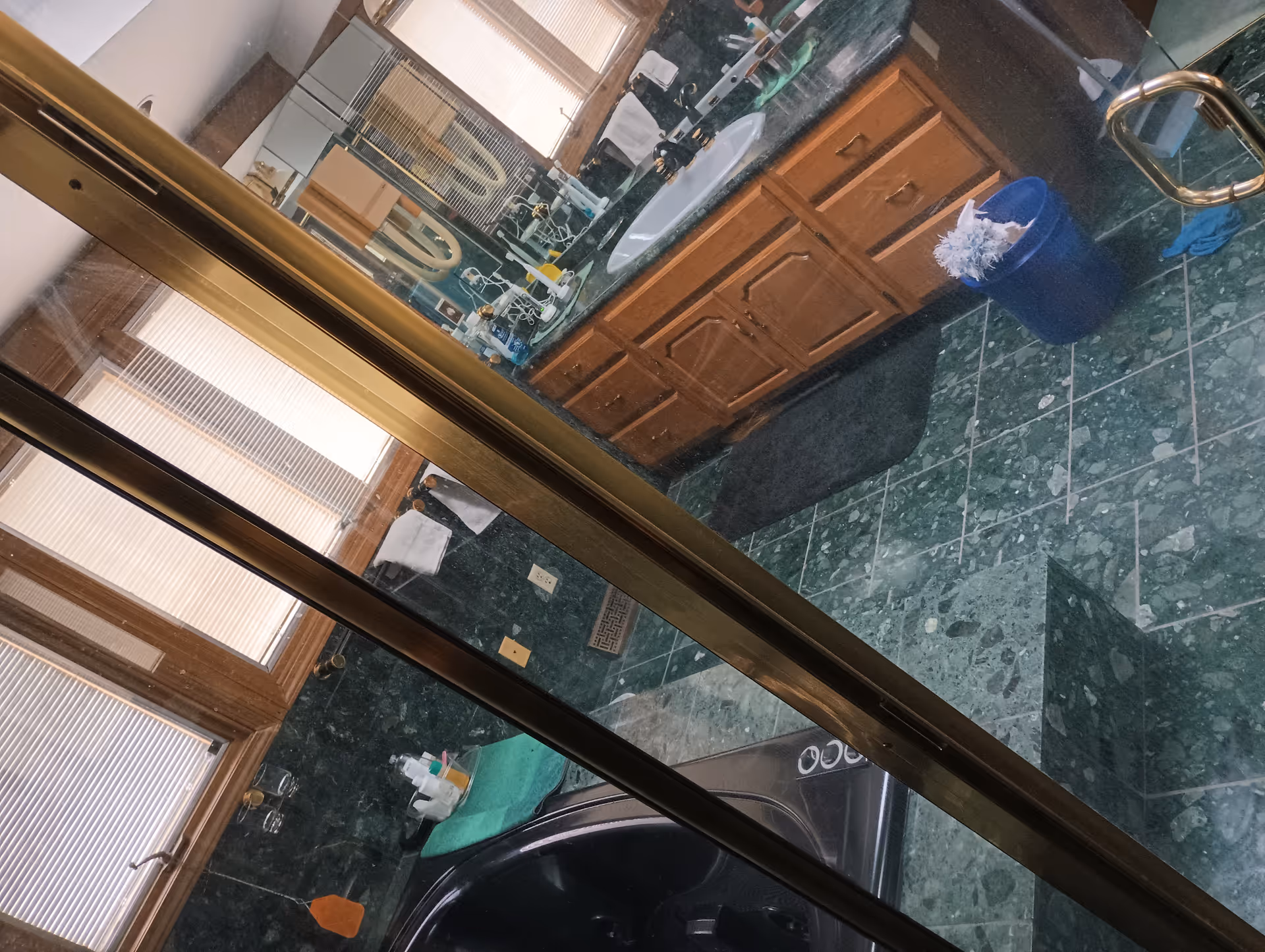 Through glass, a bathroom vanity area with wooden cabinets, green marble floor, and cleaning supplies.