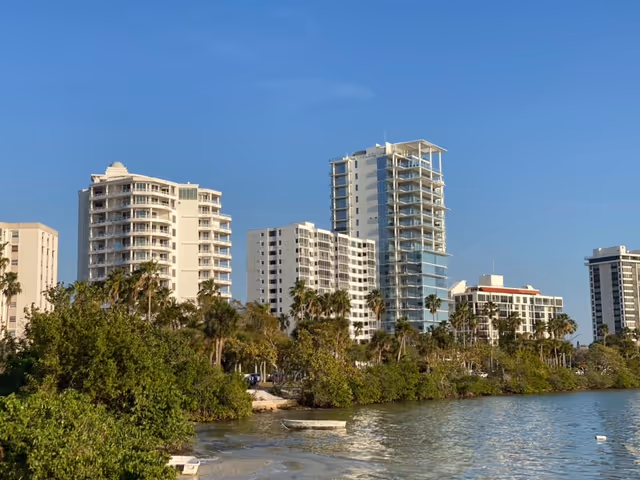 High-rise residential buildings along a waterway with palm trees and blue sky.