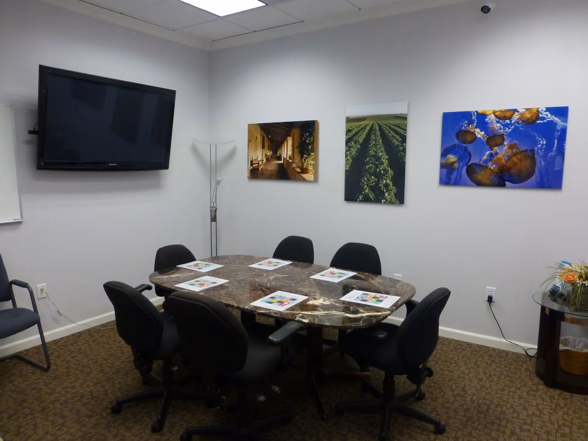 A conference room with a marble table, black chairs, wall-mounted TV, and art on the walls.