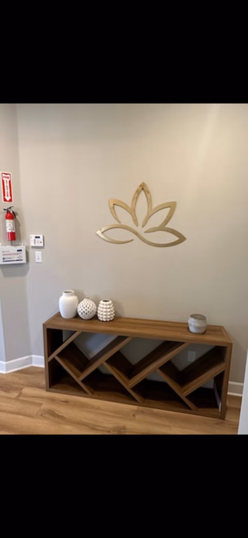 Wooden console with geometric shelves and decorative vases against a lotus wall design.