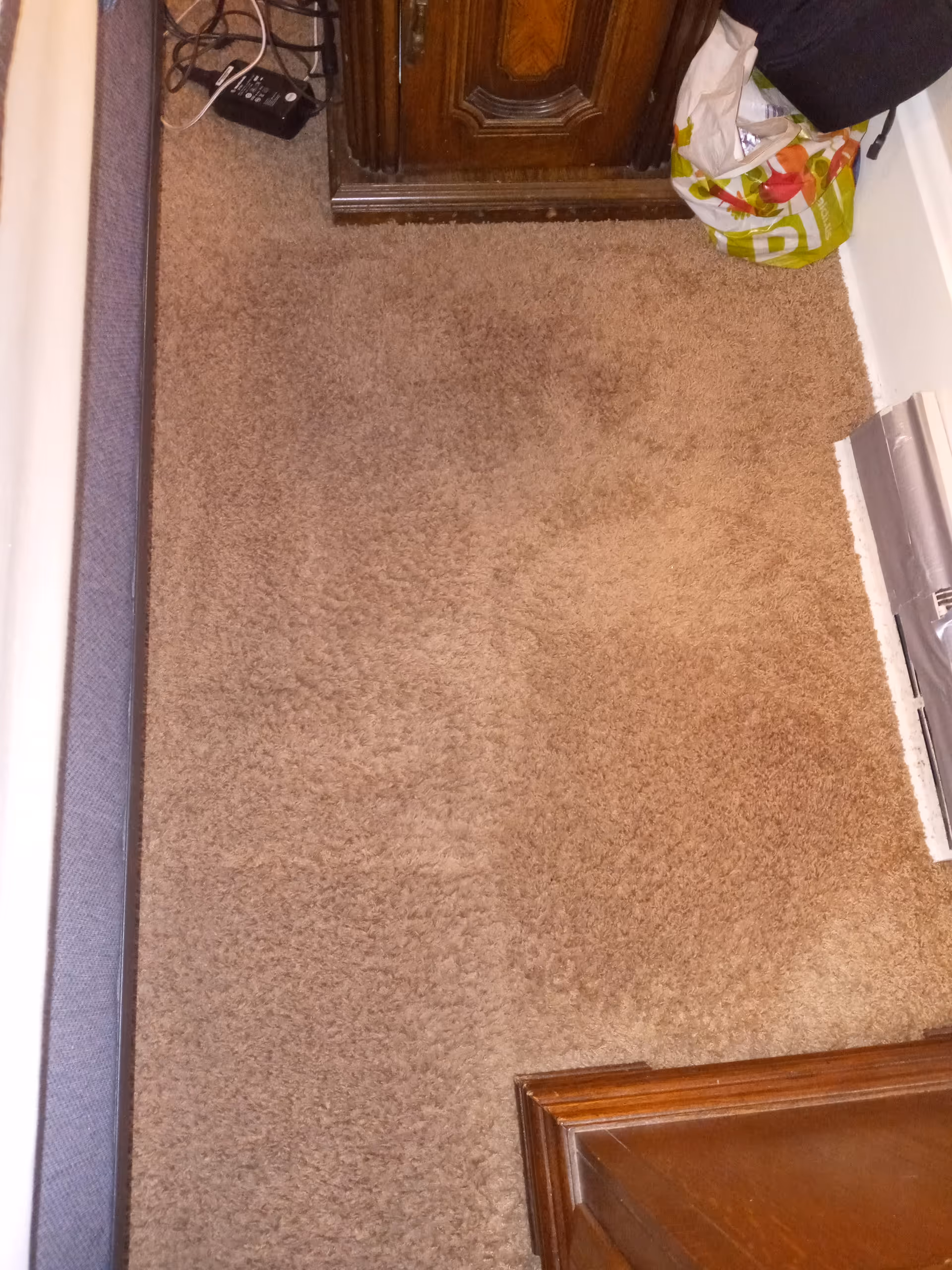 Close-up view of a carpeted hallway with a wooden cabinet and cluttered corner.