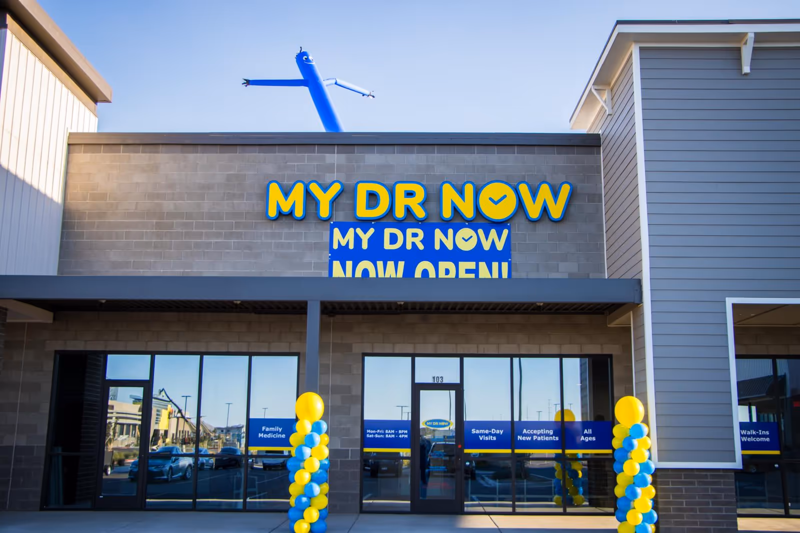 Front view of MY DR NOW building with blue and yellow sign, balloons, and open banner.