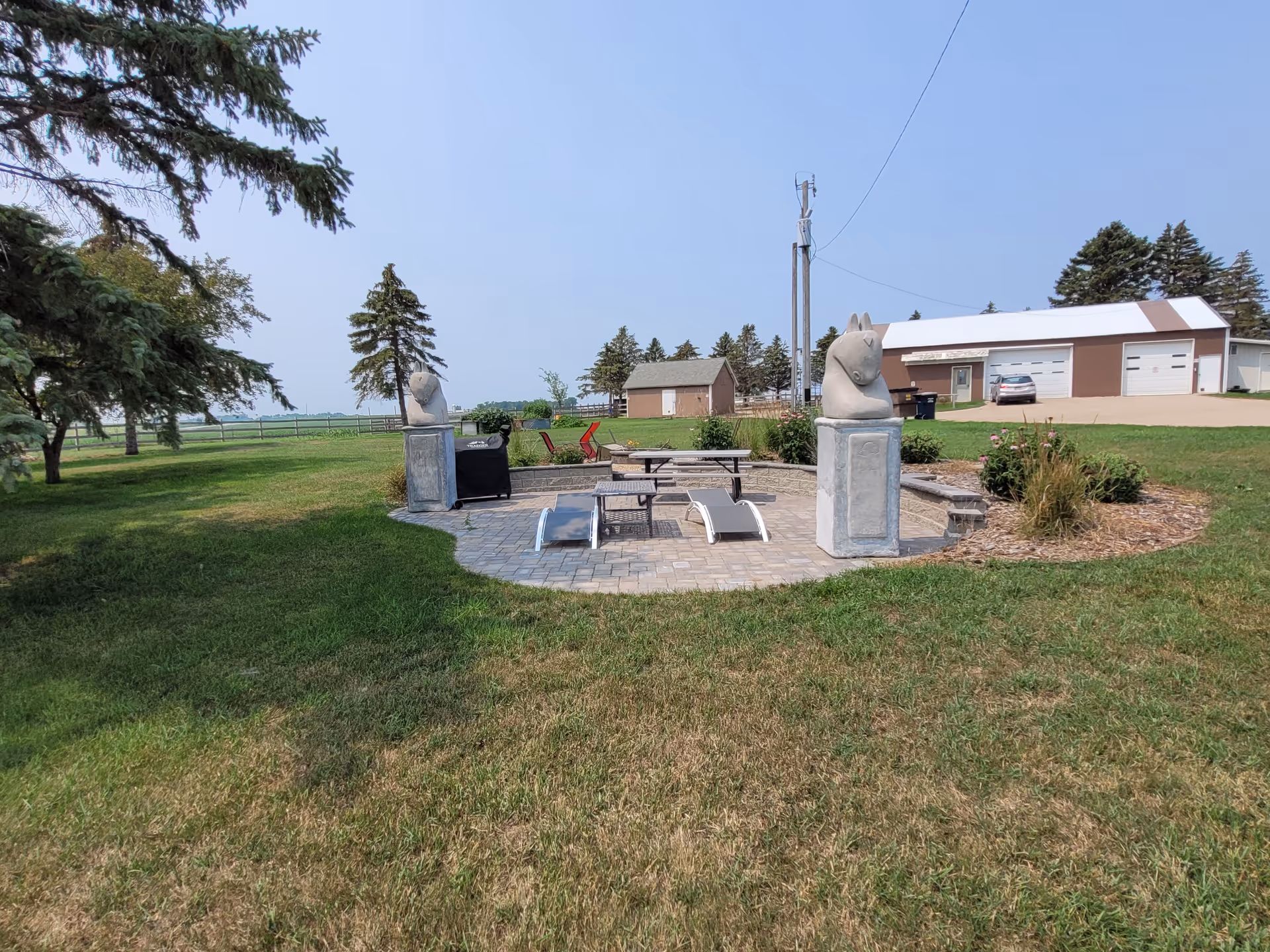 Outdoor patio with a table, chairs, and stone rabbit statues in a grassy yard.