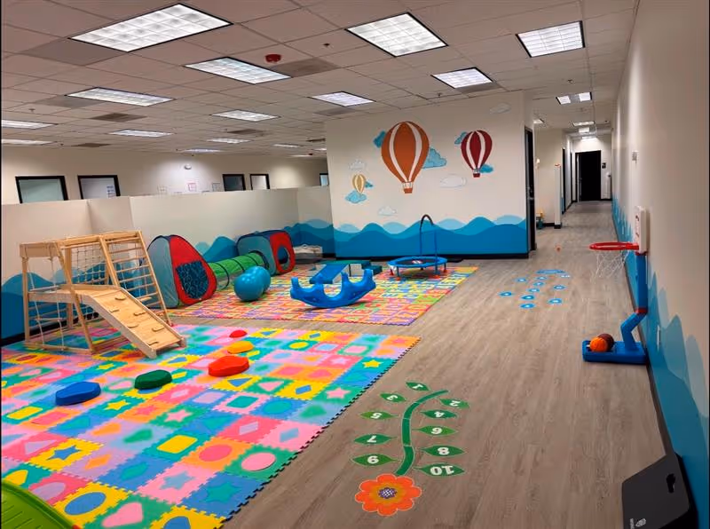 Colorful indoor play area with mats, climbing equipment, and soft toys.