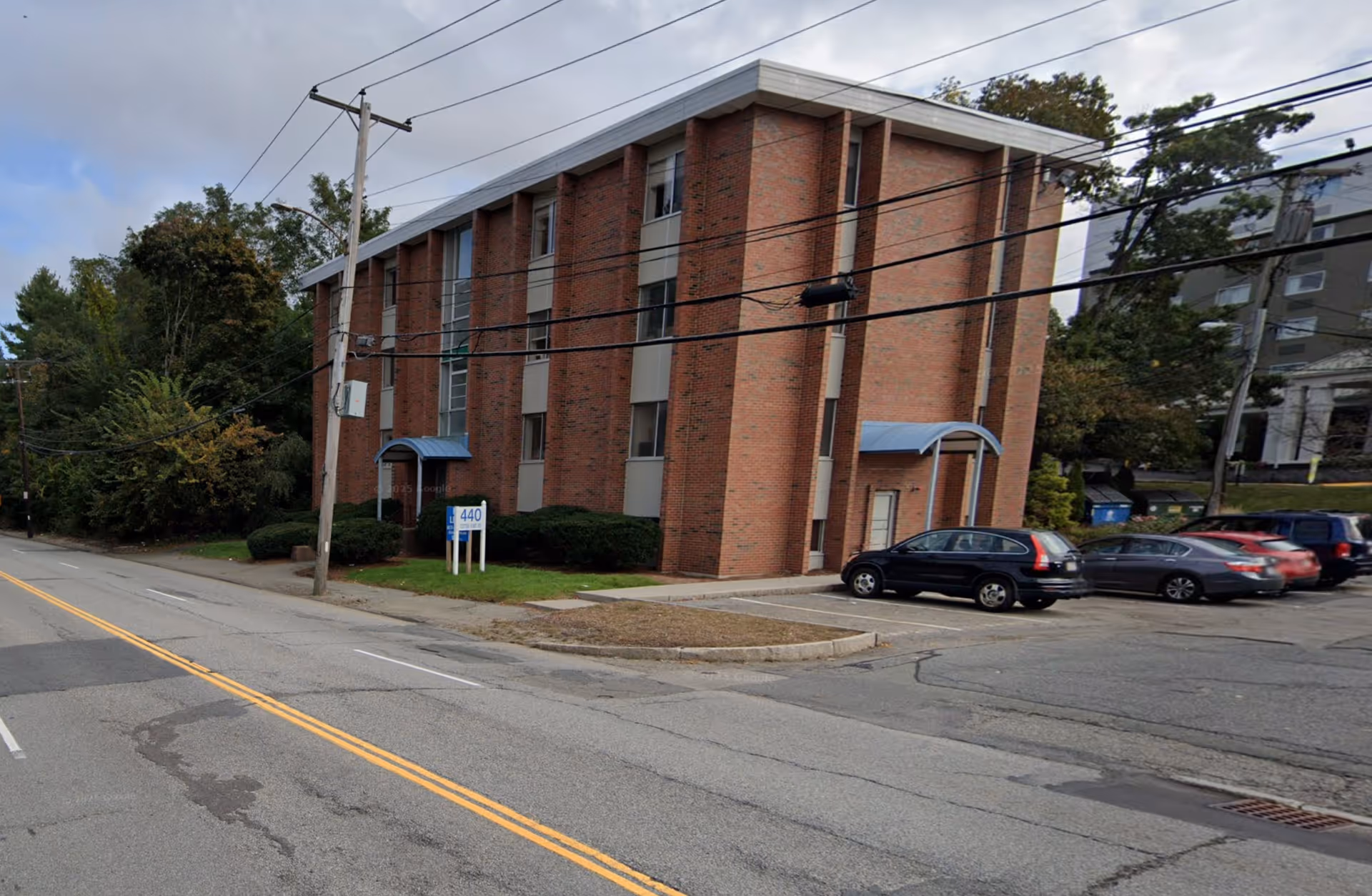 Brick senior living facility on a street with parked cars and power lines.