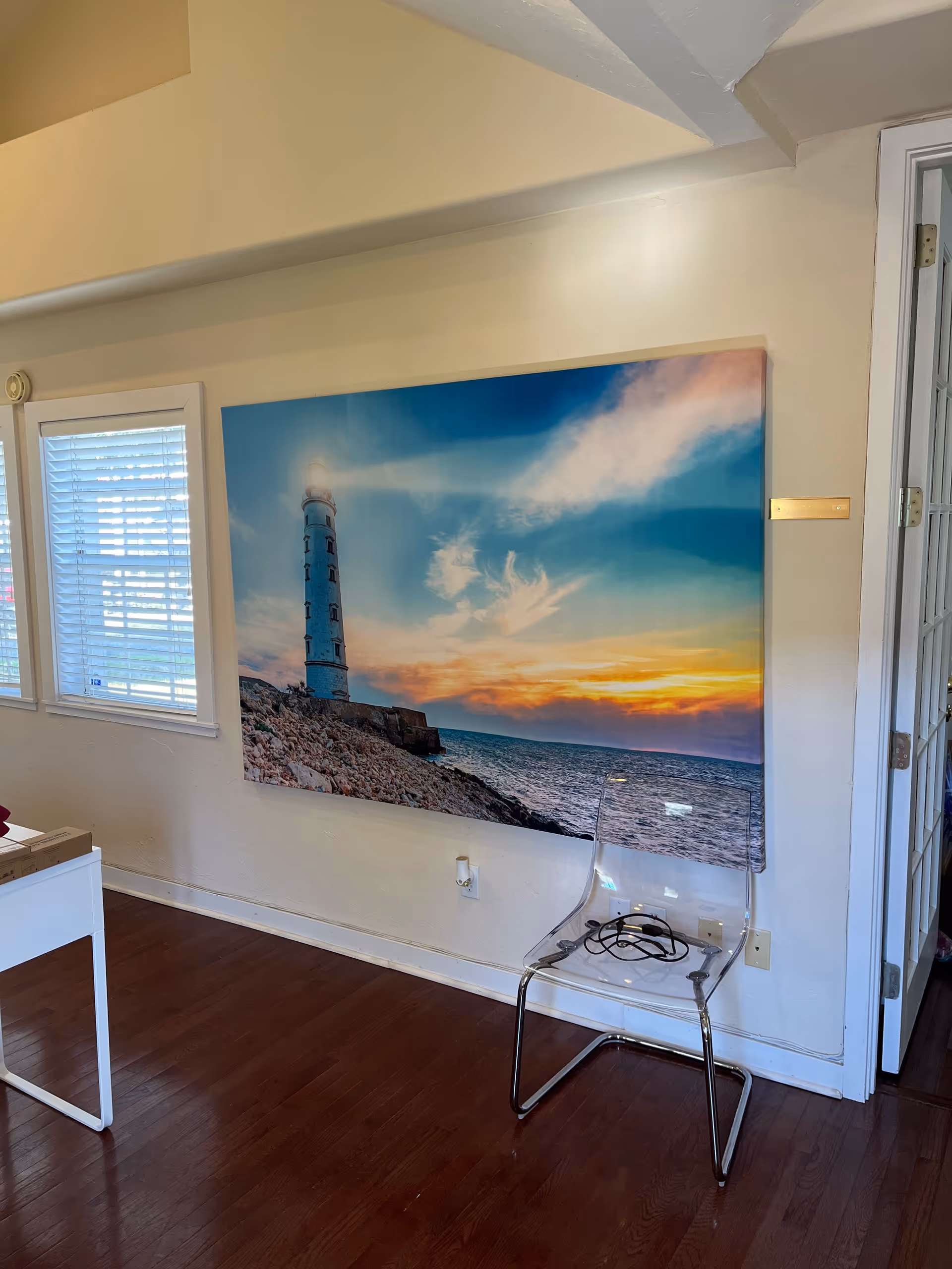 Bright interior hallway with a lighthouse canvas, wooden floor, and a clear acrylic chair.