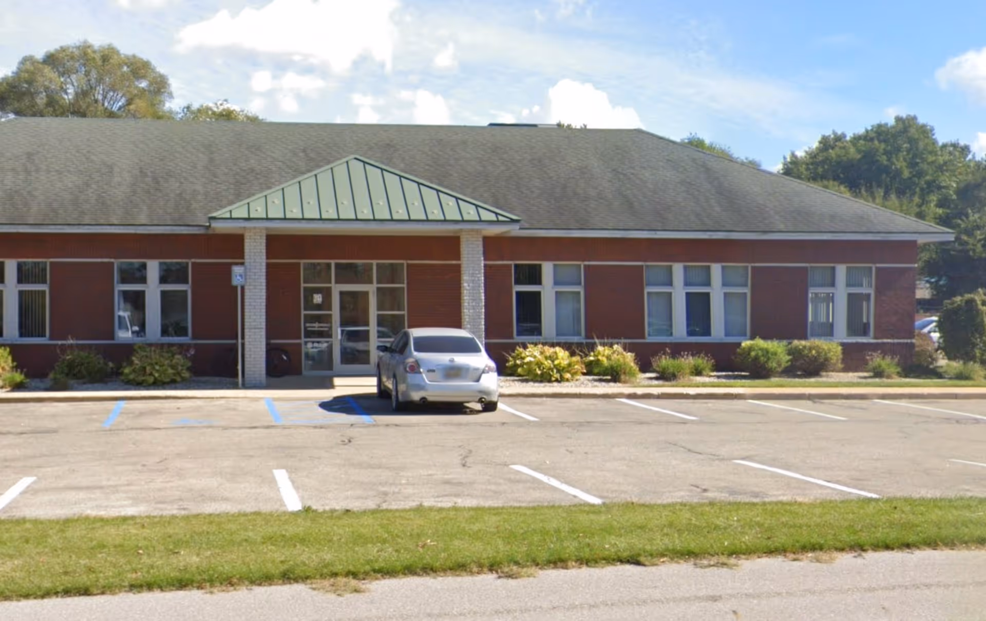 Single-story brick senior facility with front entrance and parking lot in daylight.