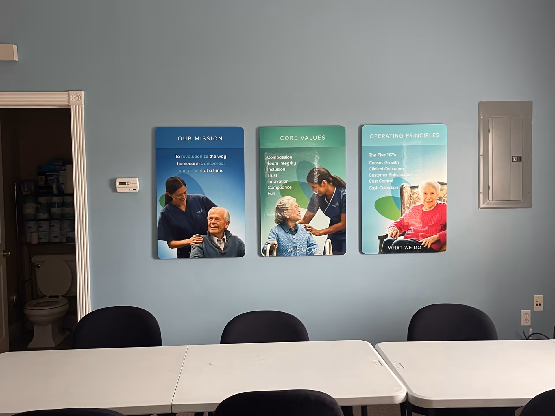 Blue-walled meeting room with three posters and a long white table.