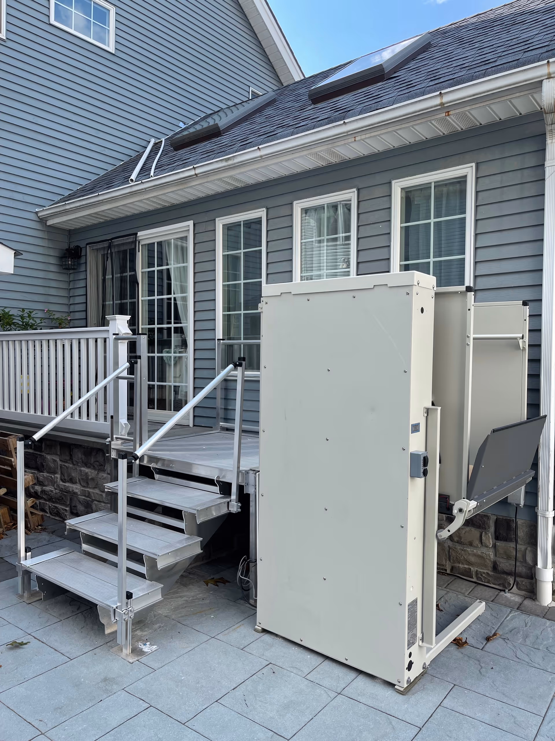 Exterior view shows a blue building with a metal outdoor stair lift on a patio.