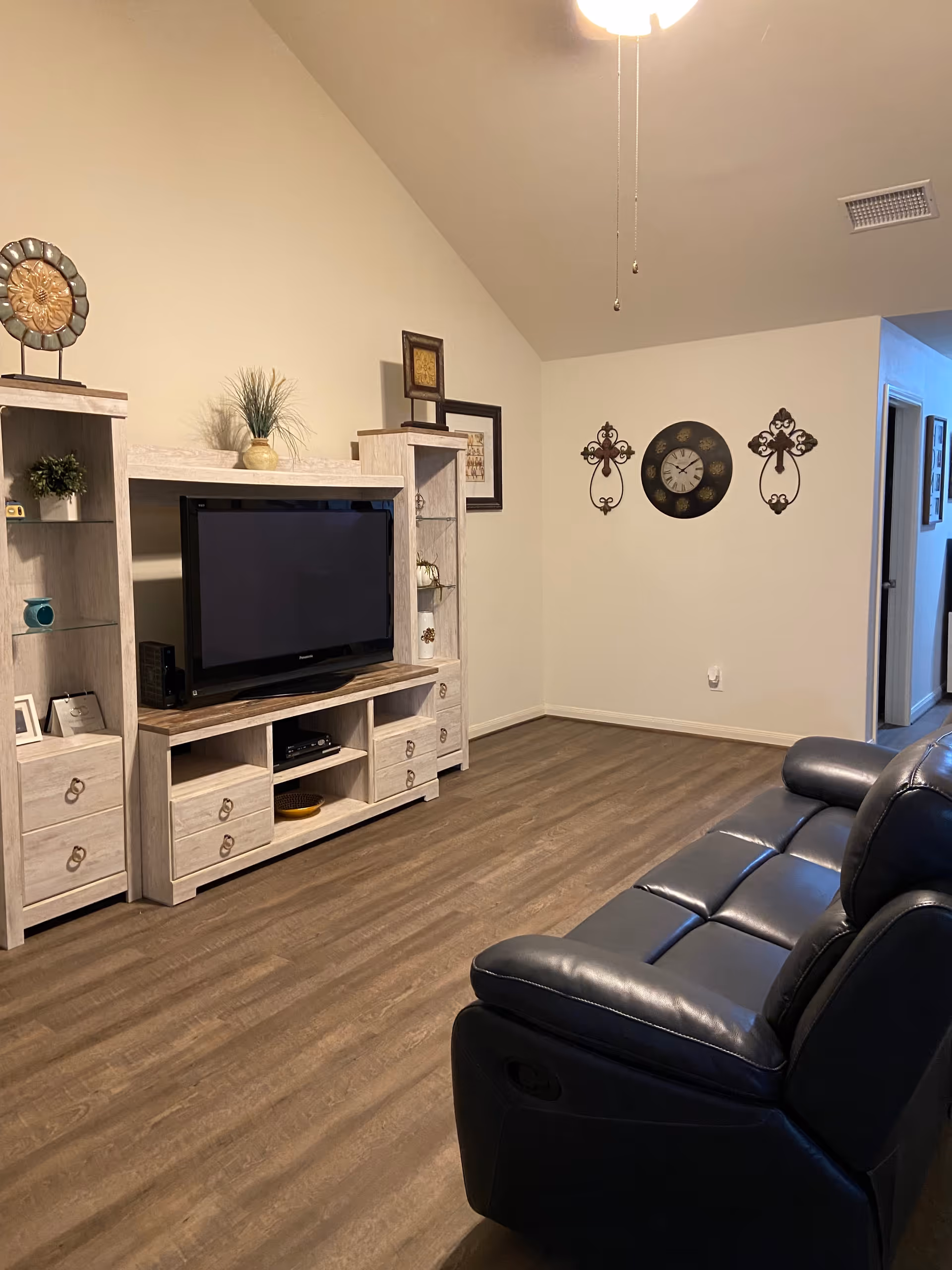 A living room with a TV on a light wood entertainment center and leather seating.