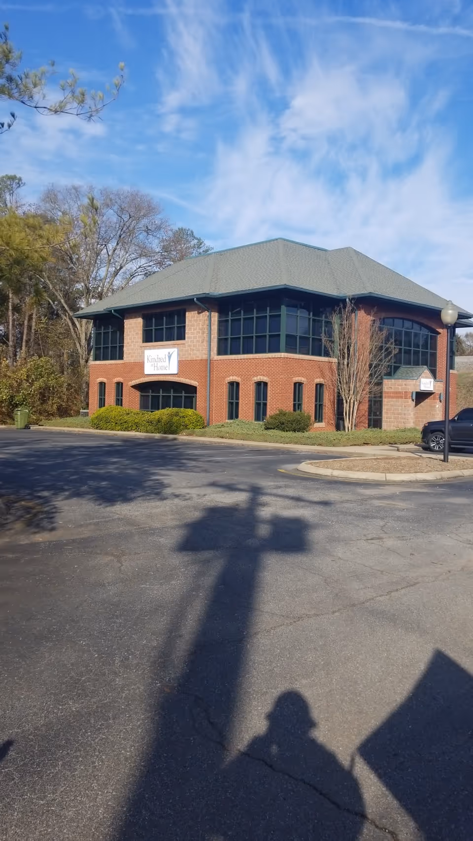 Brick two-story CenterWell Home Health building with large windows and a sign in a parking lot
