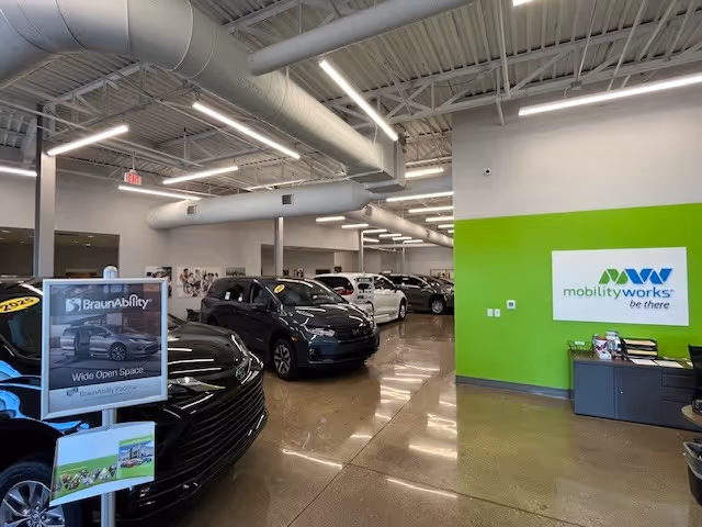 Indoor car showroom with several vehicles and a bright lime-green MobilityWorks wall.