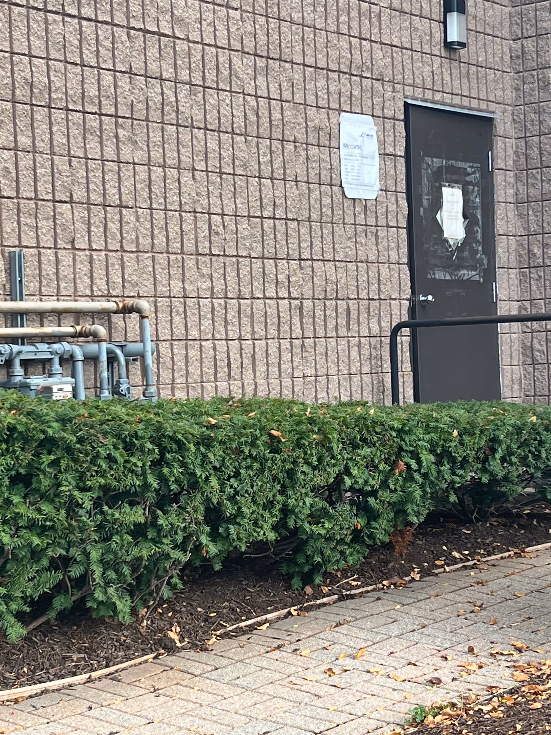 LINCARE facility exterior with brick wall, door, railing, pipes, and hedge.