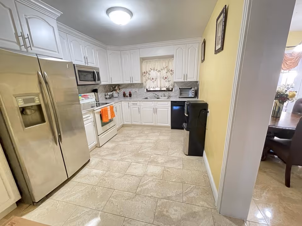 Bright white kitchen with stainless steel appliances and tiled floor beside a yellow wall.