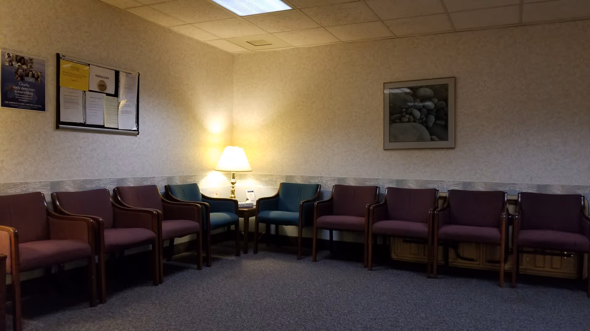 A quiet waiting area with purple and teal chairs, a lamp, and framed wall art.