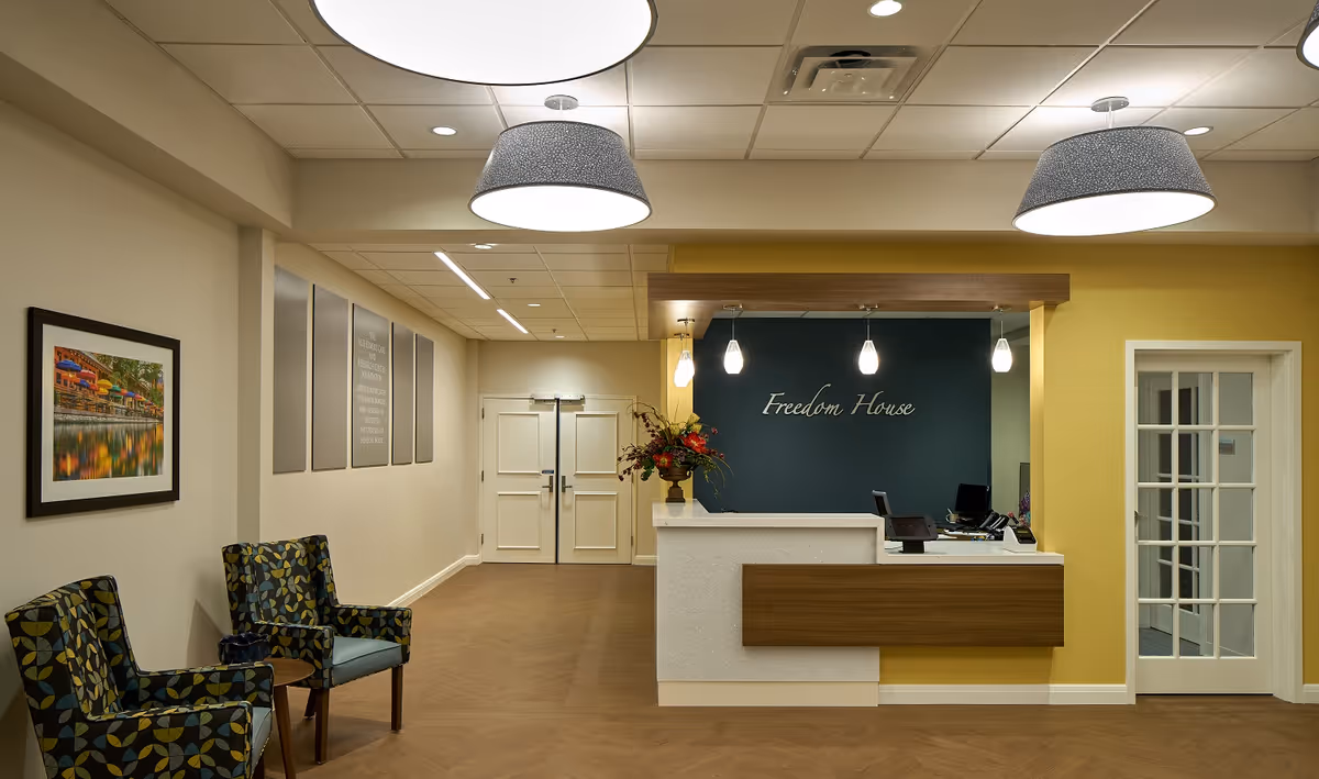 Lobby area with reception desk, seating, artwork, and a teal wall behind the Freedom House sign.