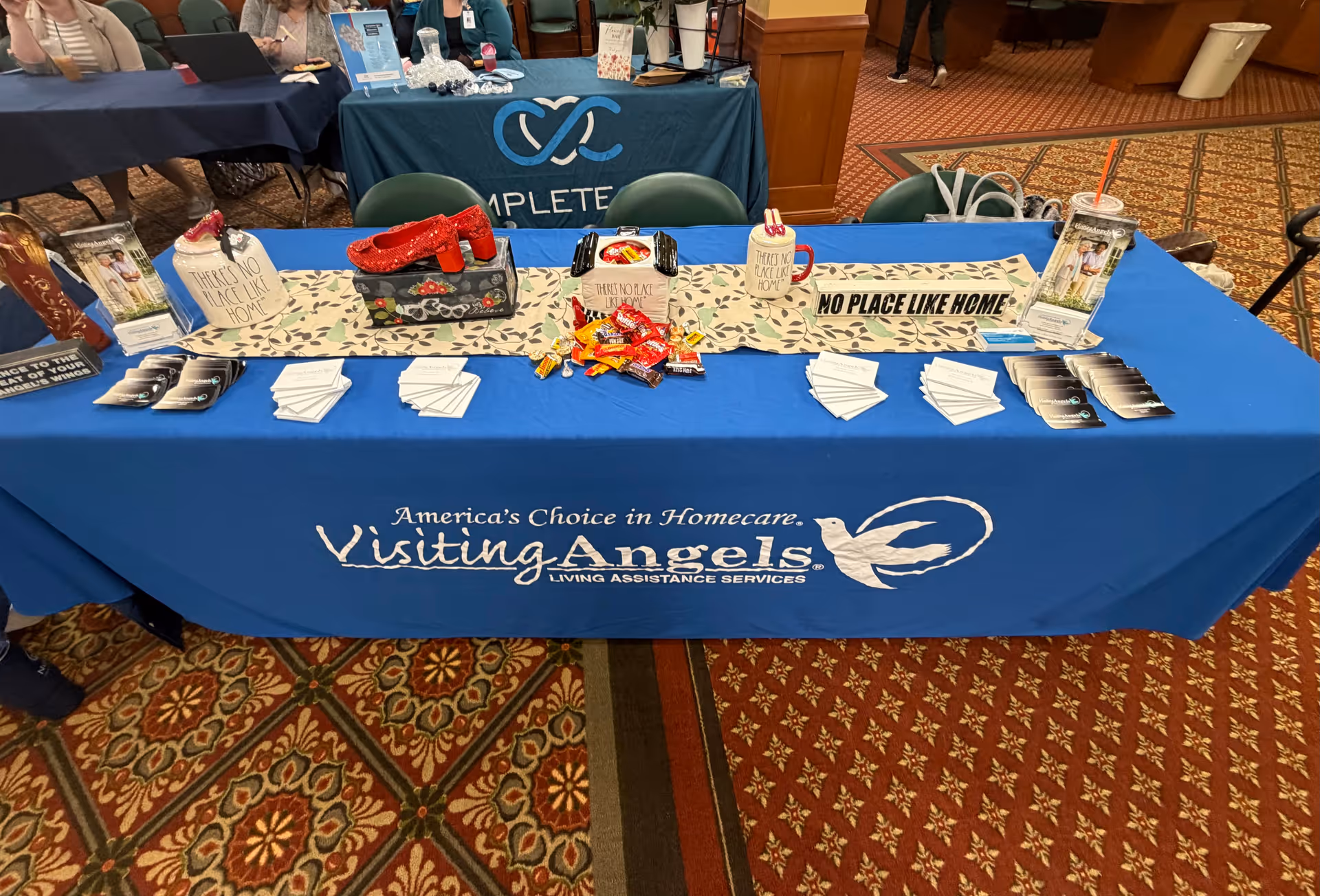 Indoor conference booth for Visiting Angels with brochures and promotional items on a blue table.