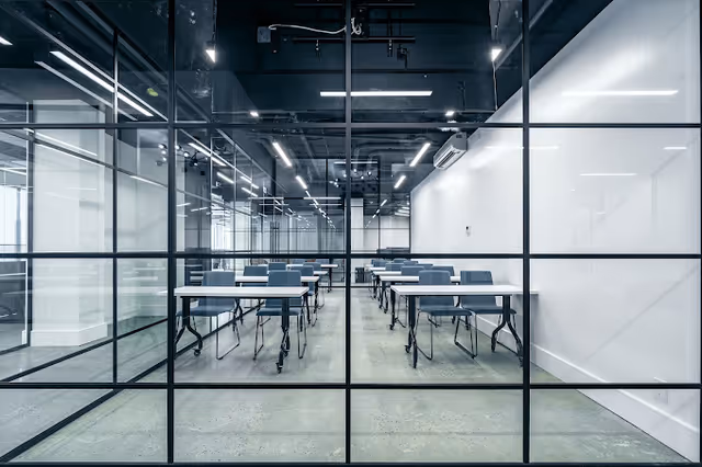 Modern glass-walled classroom with rows of desks and blue chairs inside a facility