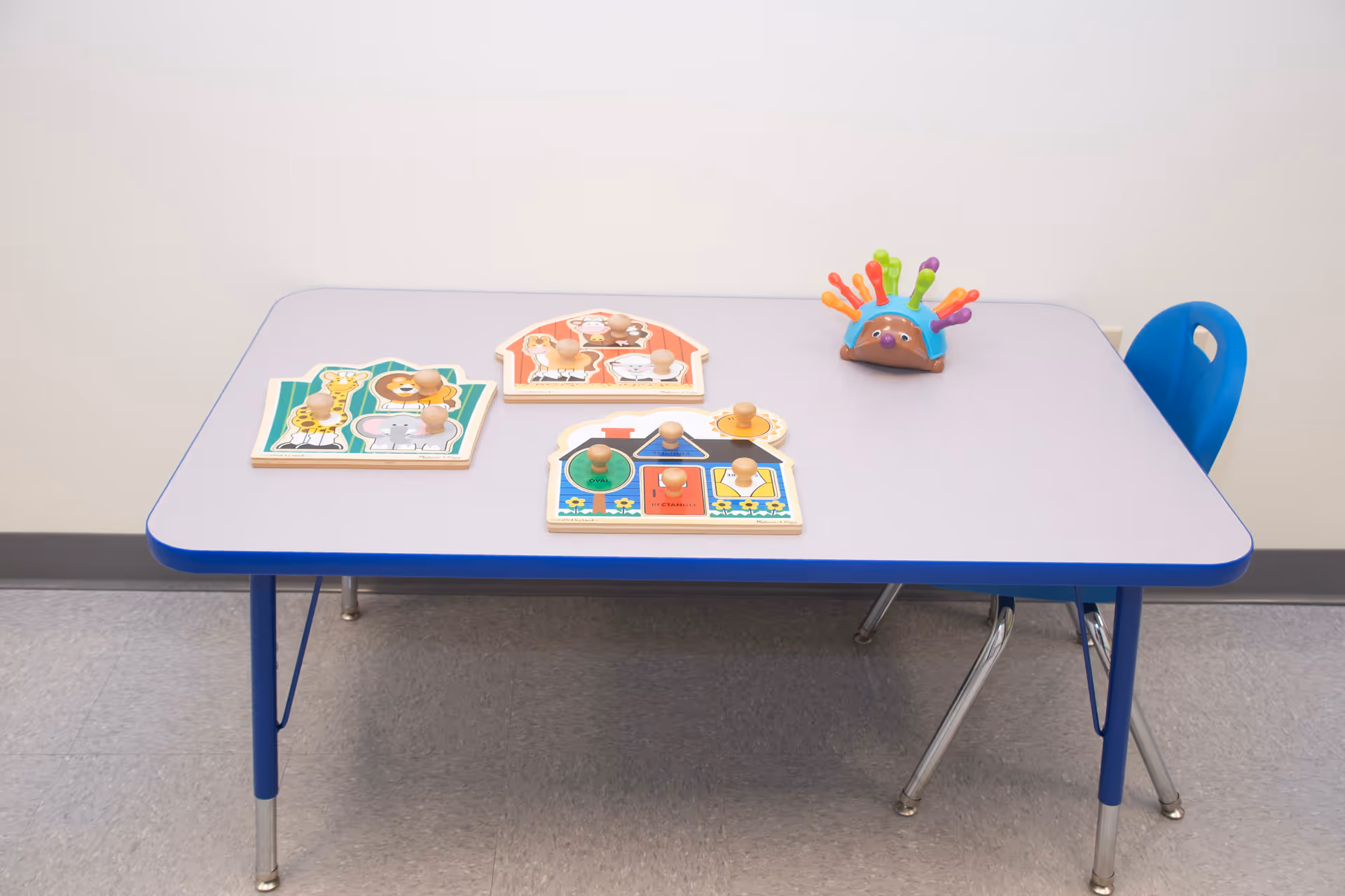 Blue children's table with puzzle boards and a colorful toy in a playroom.