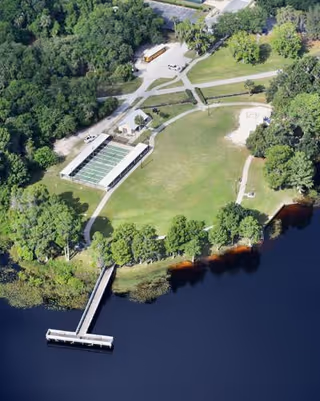 Aerial view of a waterfront senior living campus featuring a dock and green lawns.