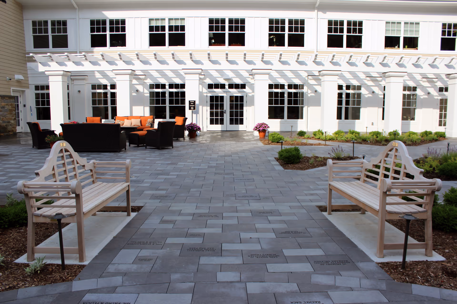 Outdoor courtyard with benches and lounge seating in front of a white hospice building.