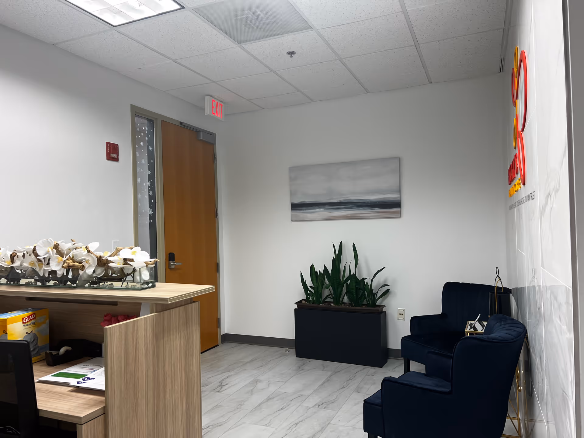 Reception lobby with a wooden desk, potted plants, and navy chairs.
