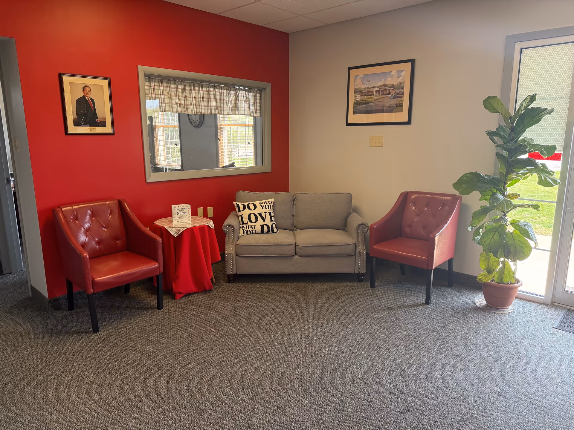 Cozy lounge area with red accent wall, seating, plant, and framed art.