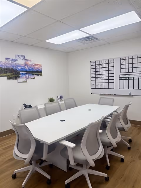 Bright conference room with a long white table, chairs, and a whiteboard.