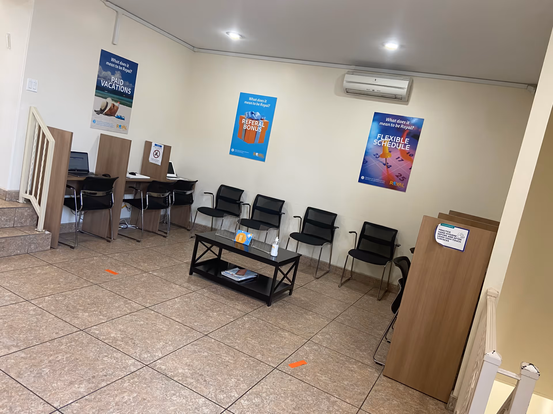 A quiet Royal Care lobby with cubicles, chairs, posters, and a coffee table.