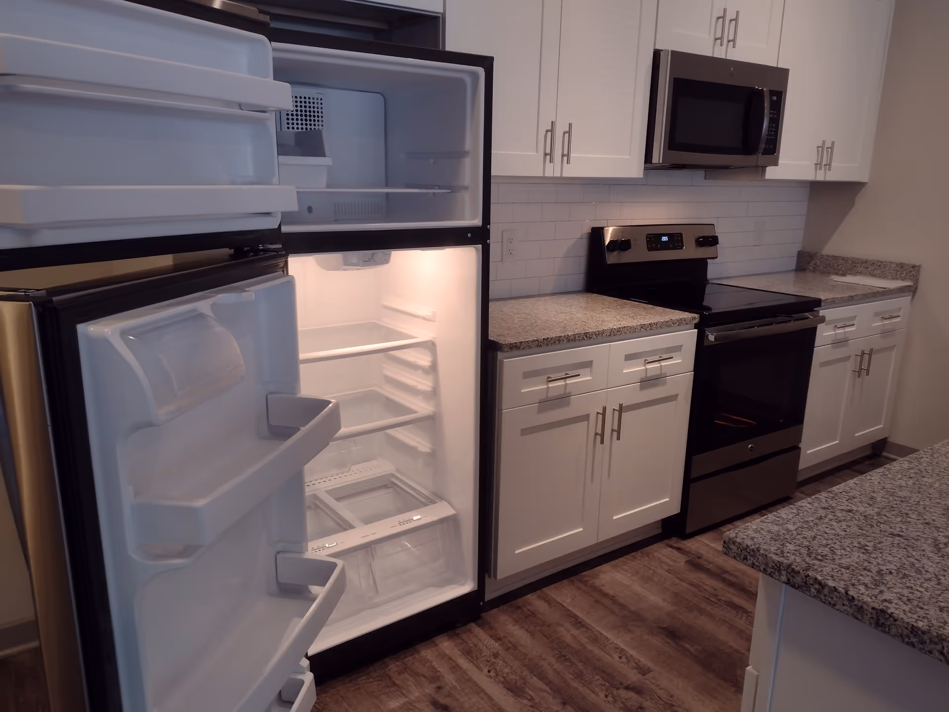 Open refrigerator in a modern white kitchen with stove, microwave, and granite countertops.
