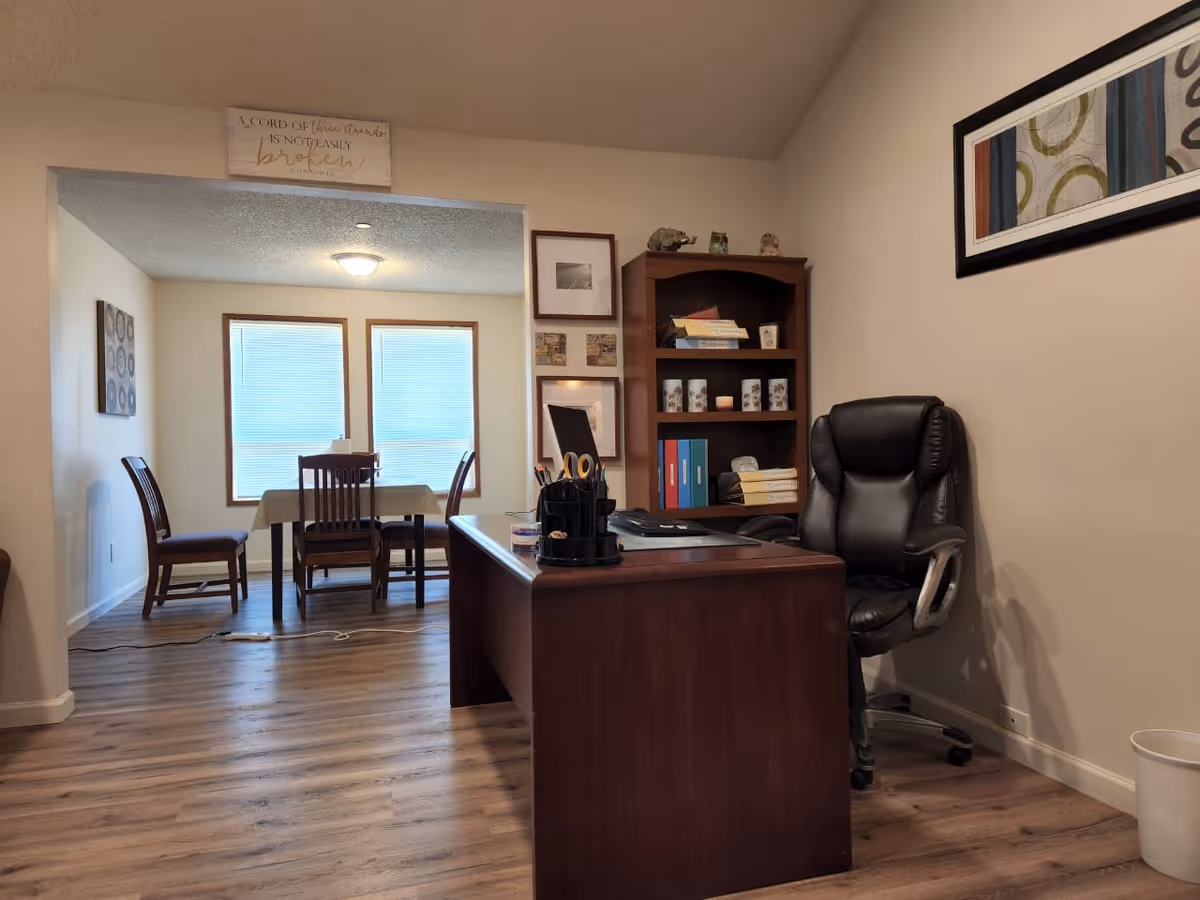 Office desk in foreground with chair and bookshelf; dining table visible beyond.