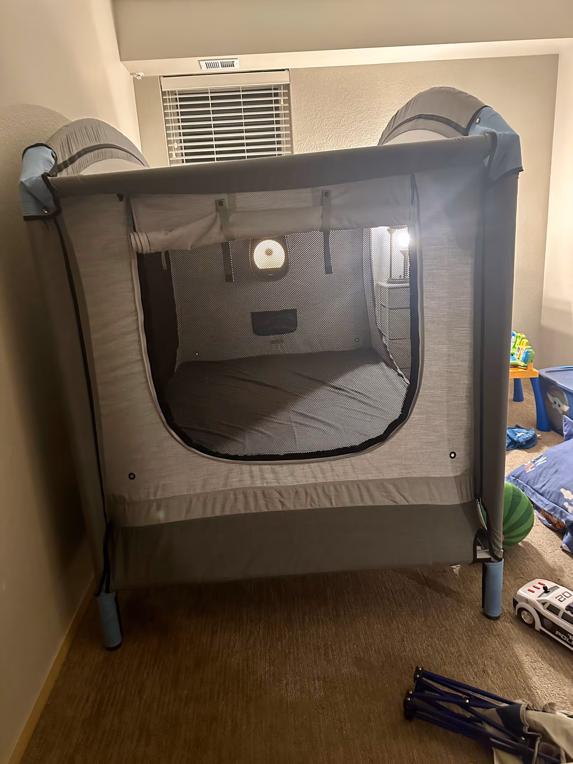 Gray portable playpen set up in a small room with toys nearby.