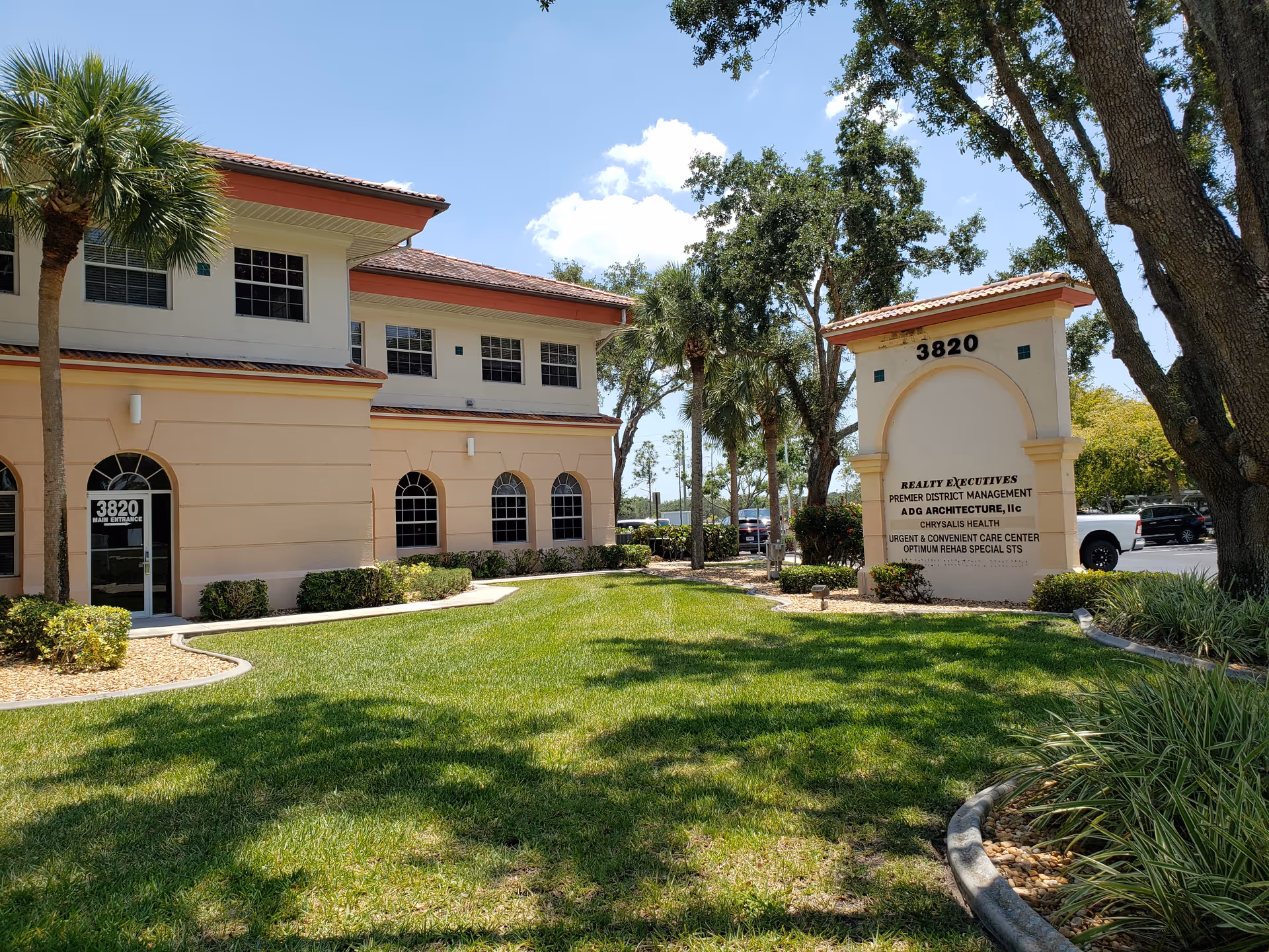 Sunlit two-story beige building with arched windows, palm trees, and a front entrance sign.