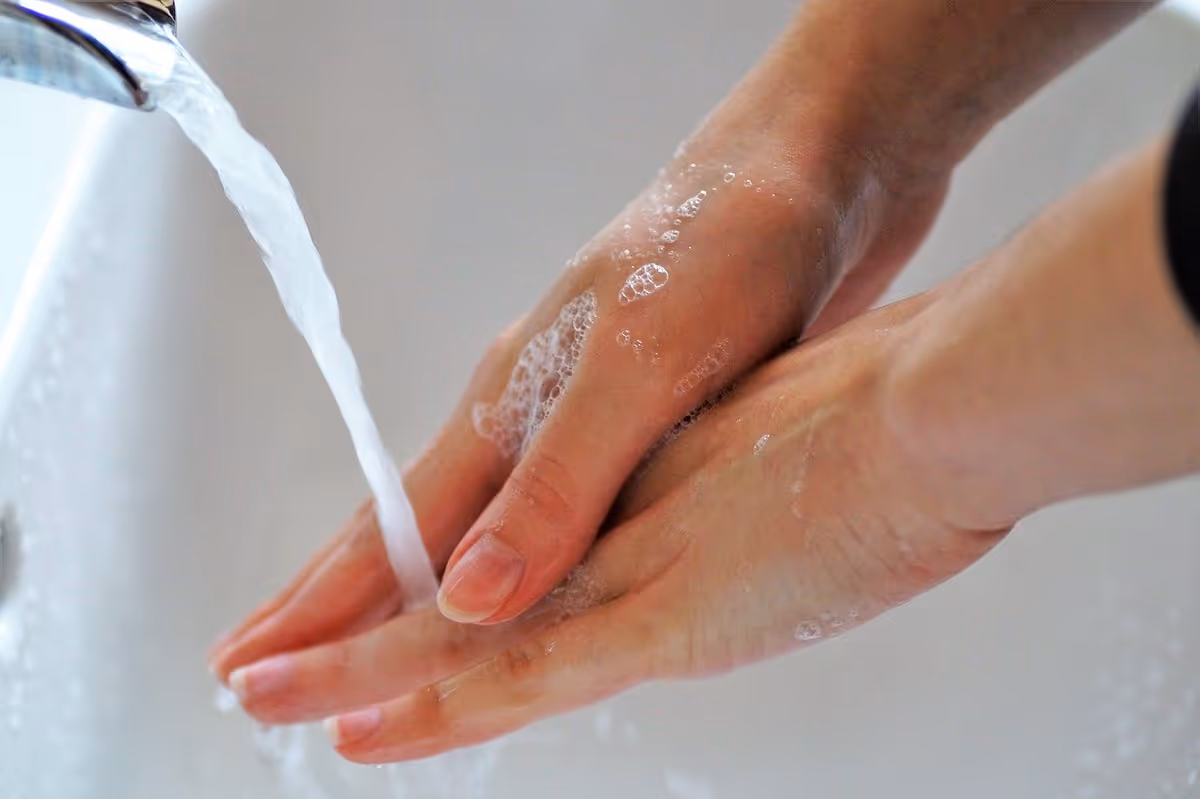 Hands washing under running water at a bathroom sink with soap suds