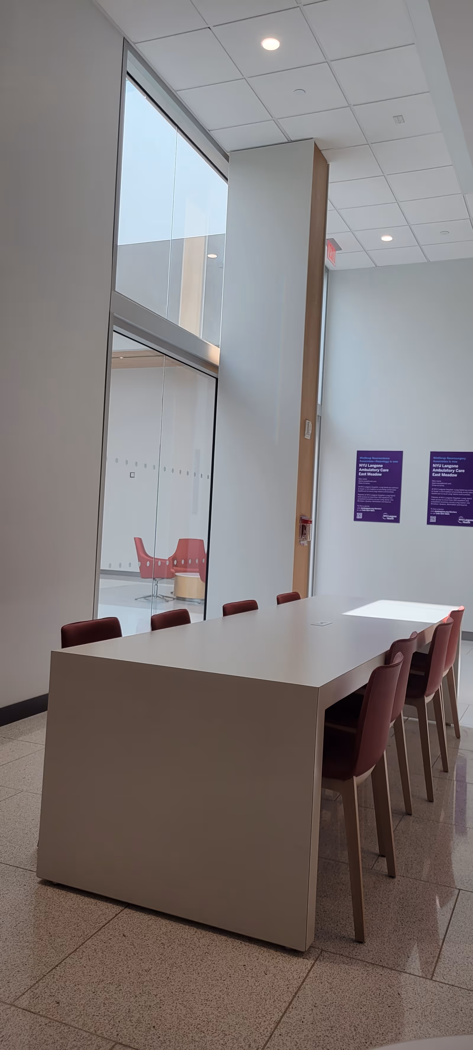Interior of NYU Langone Ambulatory Care East Meadow with a long white table and red chairs.