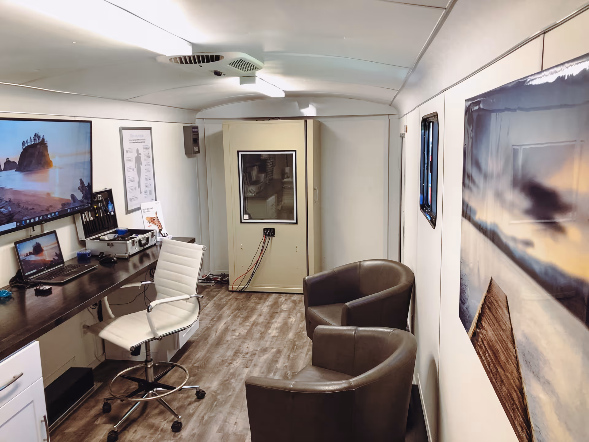 Interior of a mobile hearing center: desk with laptop, exam chair, and two brown lounge chairs.