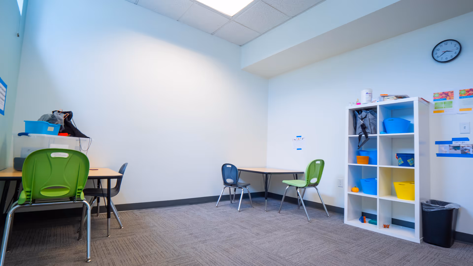 Bright, empty activity room with small tables, colorful chairs, and cubby shelving.