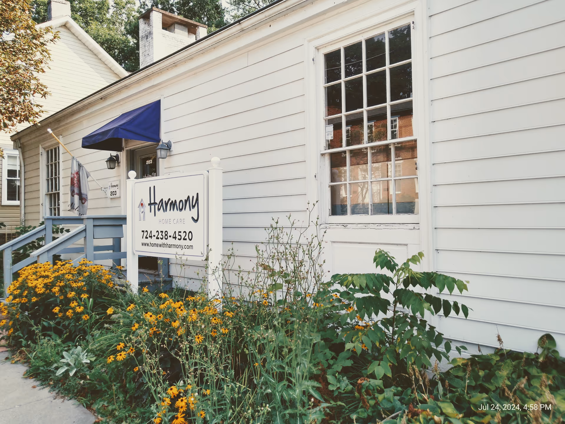 Exterior view of Harmony Home Care building with sign and yellow flowers.
